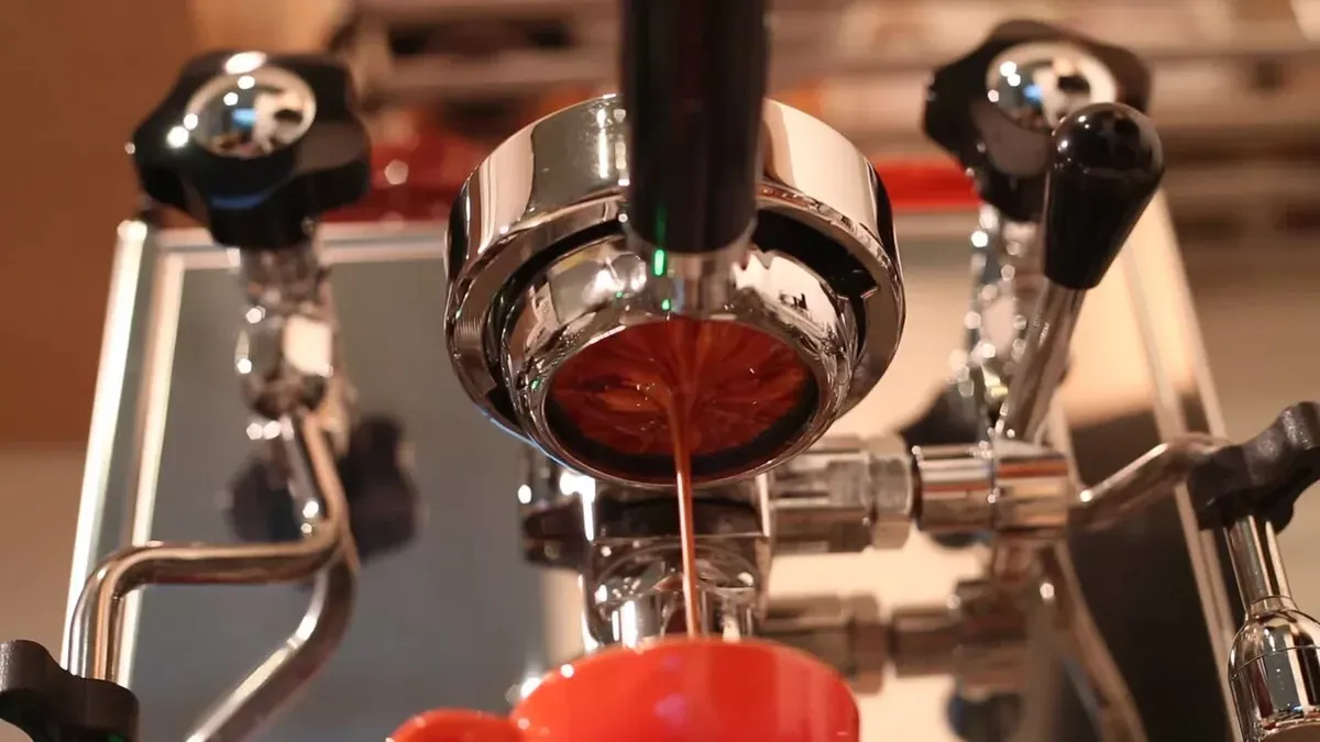 Espresso streaming from a bottomless portafilter into a red cup on a home espresso machine