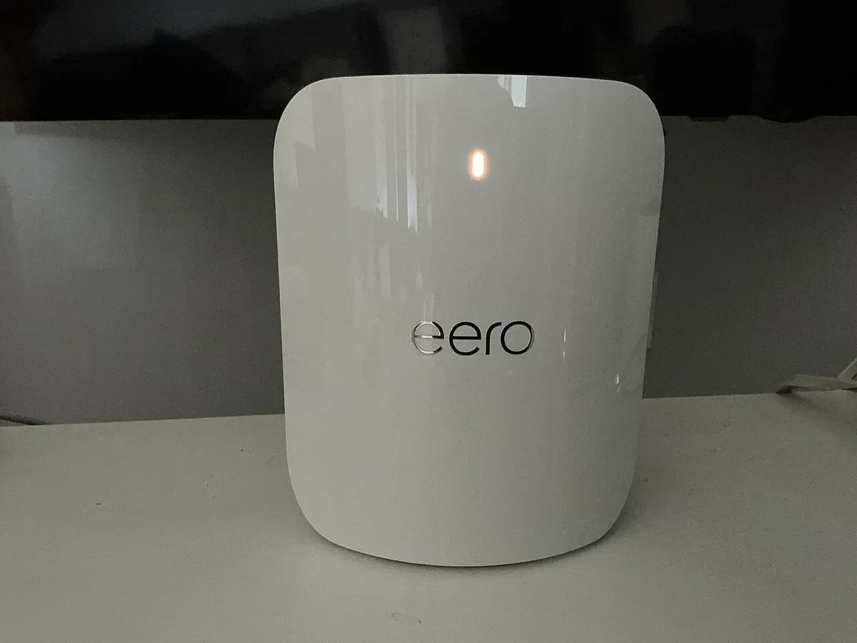 A white eero Pro 7 mesh Wi-Fi router with a small status light, standing on a shelf