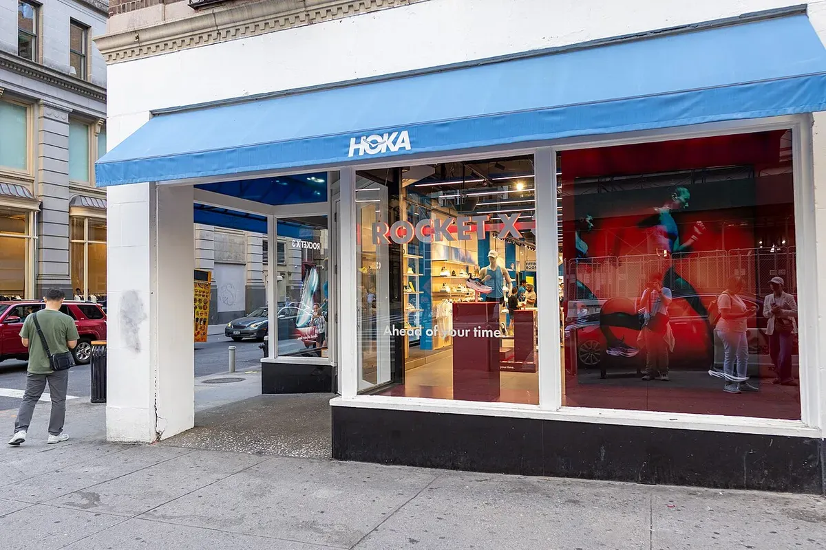 The front of a HOKA store with a blue awning on a street corner in New York City