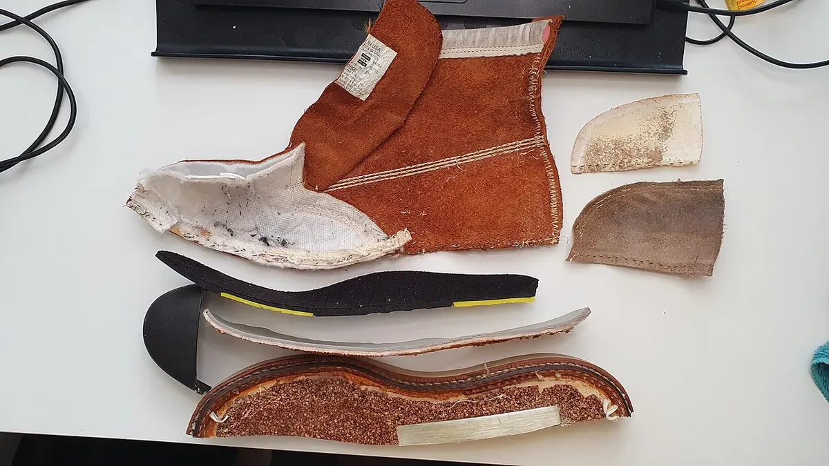 A Thorogood moc toe safety boot cut apart to show its leather upper, steel toe cap, footbed, insole, and wedge sole
