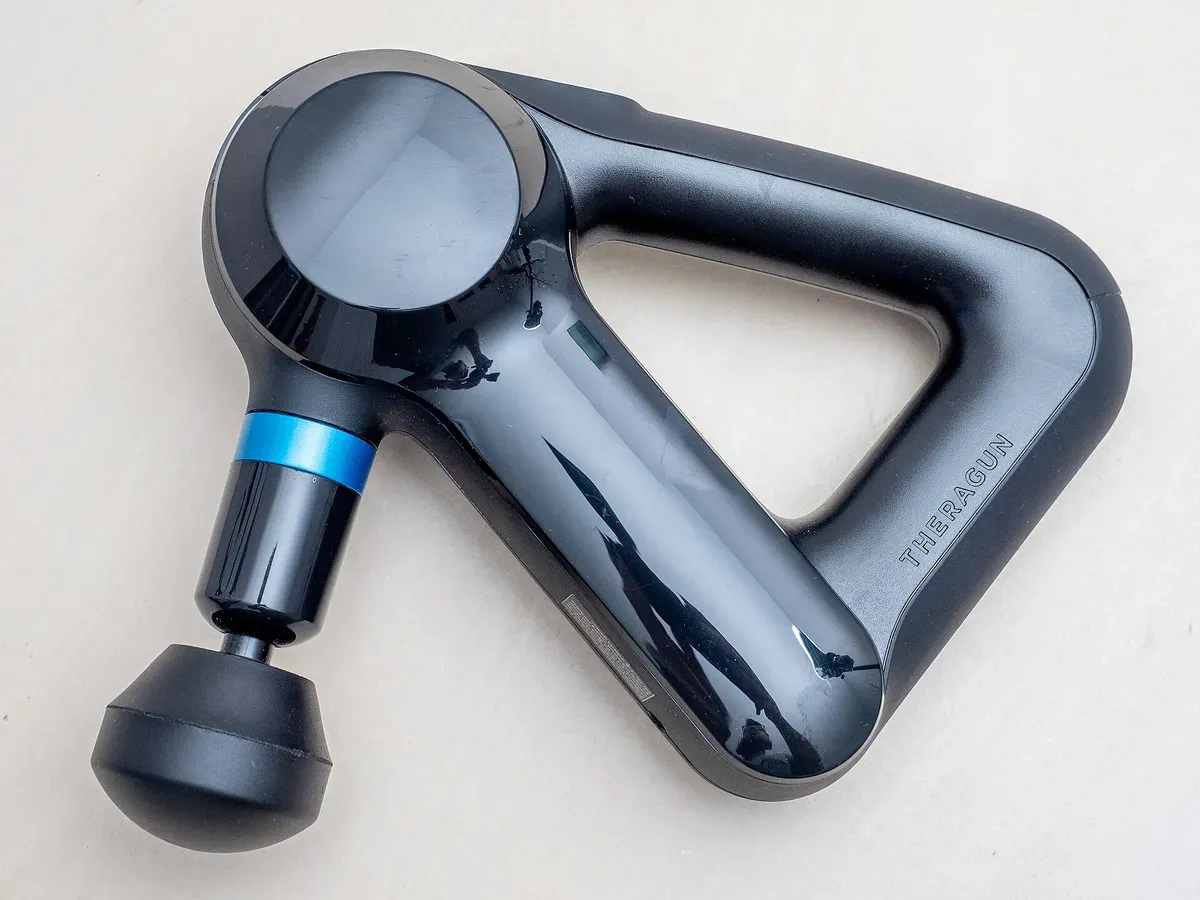 A Theragun massage gun with a triangular handle and a ball attachment, resting on a table