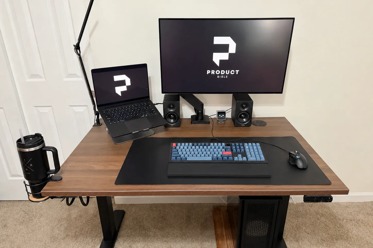 The UPLIFT V3 standing desk set up with a laptop stand, Dell monitor, speakers, keyboard, mouse, and cup holder