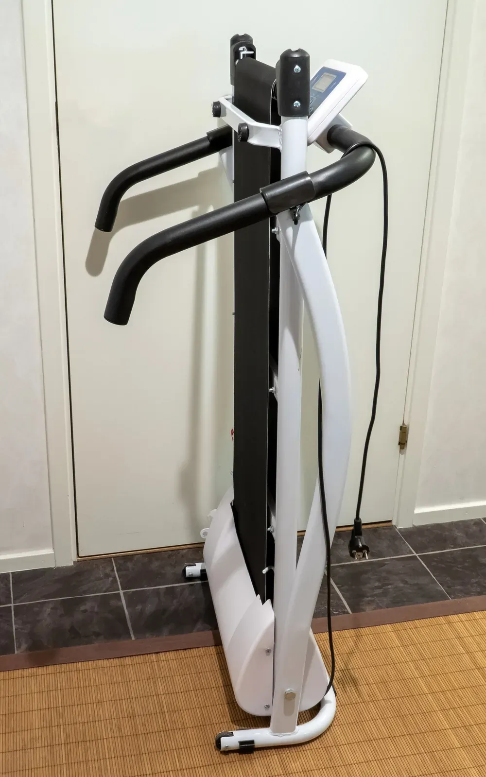 A white home treadmill folded upright against a wall, with its handrails and console still attached